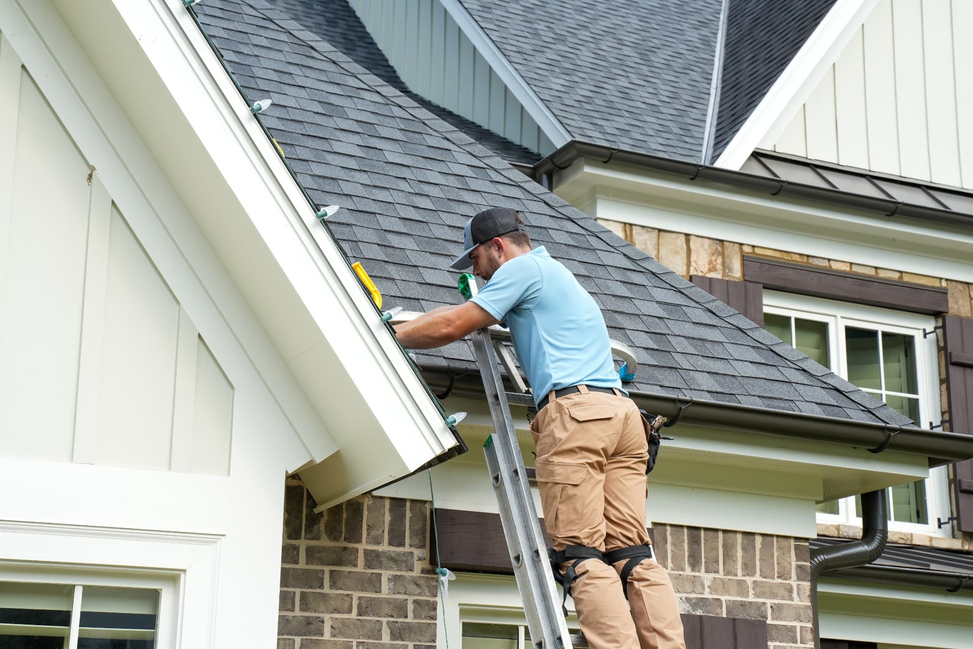 Crew member clipping Christmas lights along a roofline
