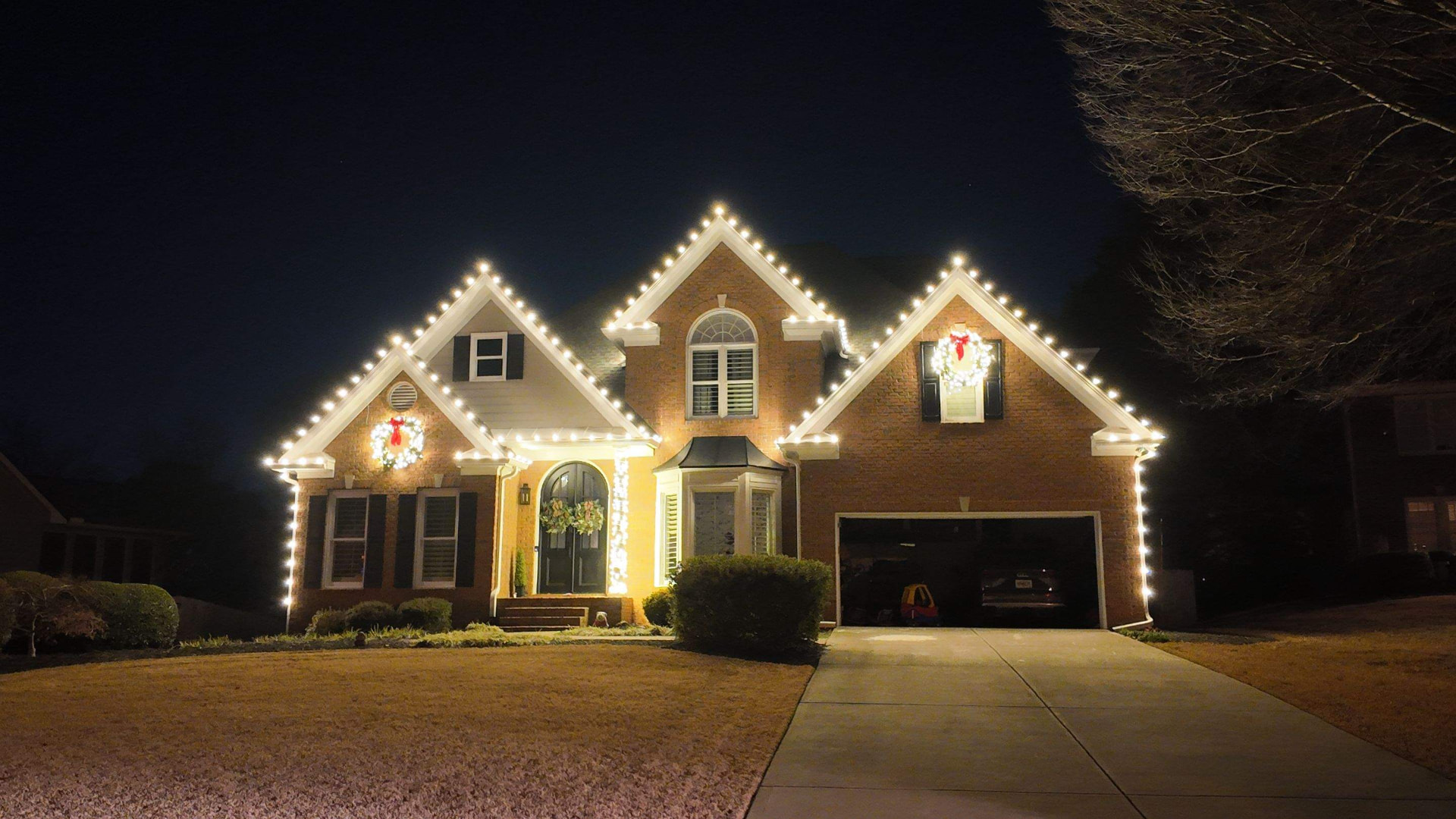 Brick home with warm roofline Christmas lights and a glowing wreath