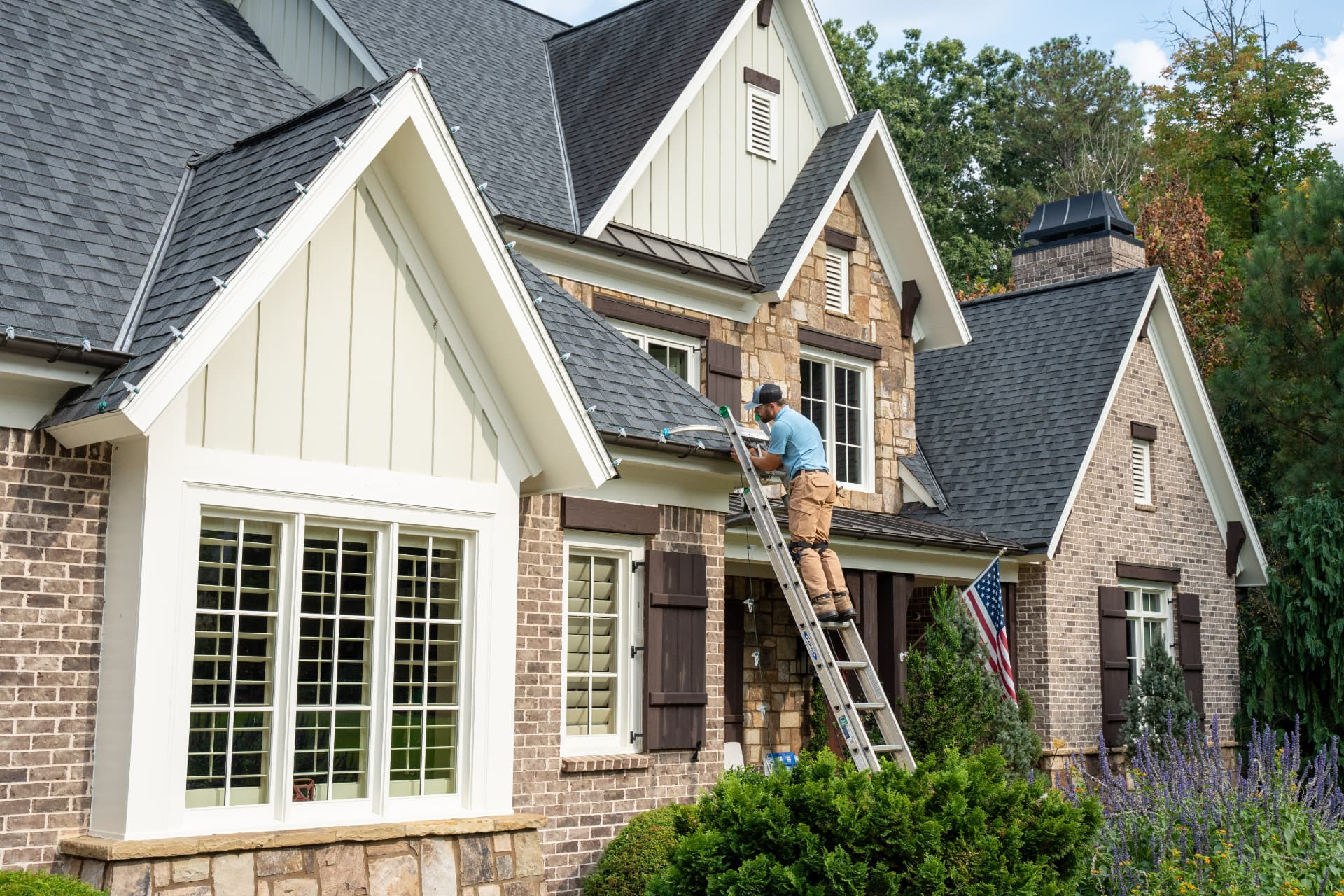 Installer on a ladder clipping Christmas lights to a gutter line
