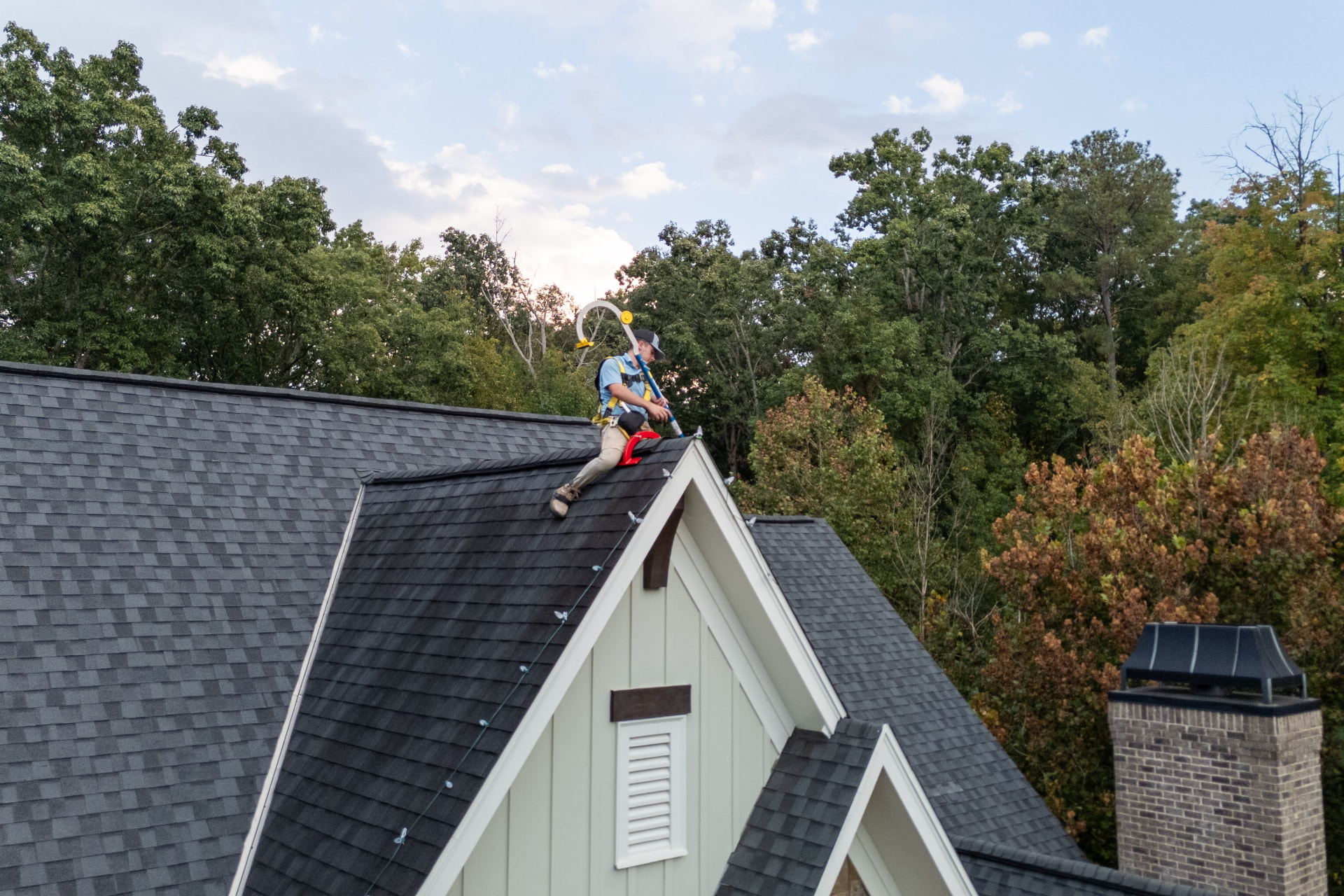 Installer setting Christmas lights along a steep roof peak at dusk