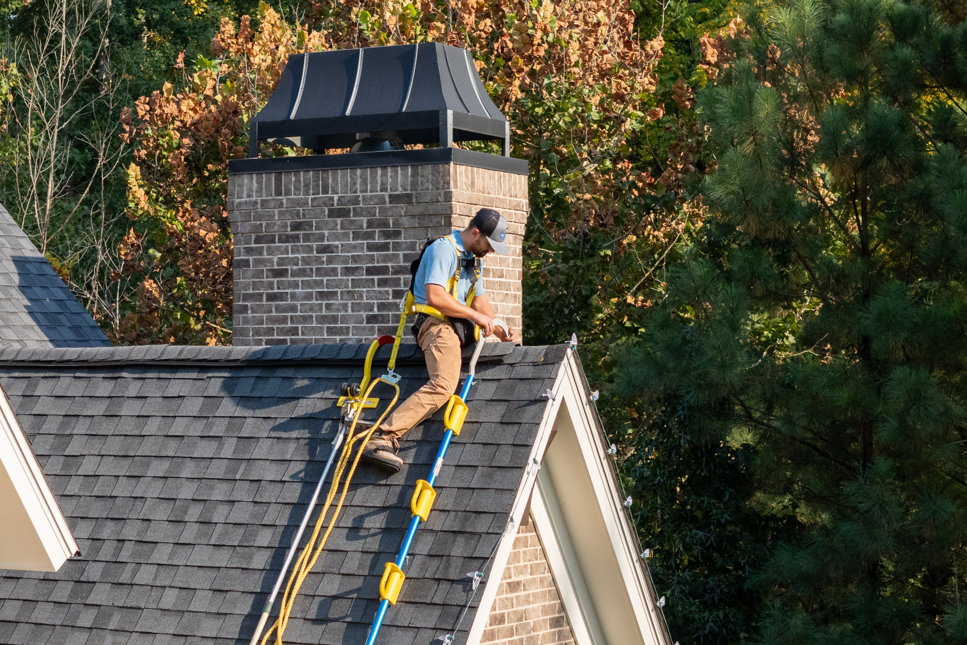 Harnessed installer running Christmas lights along a roof ridge by the chimney