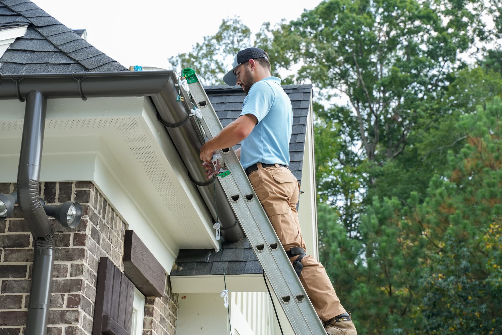 Crew member installing roofline Christmas lights from a ladder